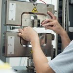 Technician loading a test specimen into the grips of a universal testing machine.
