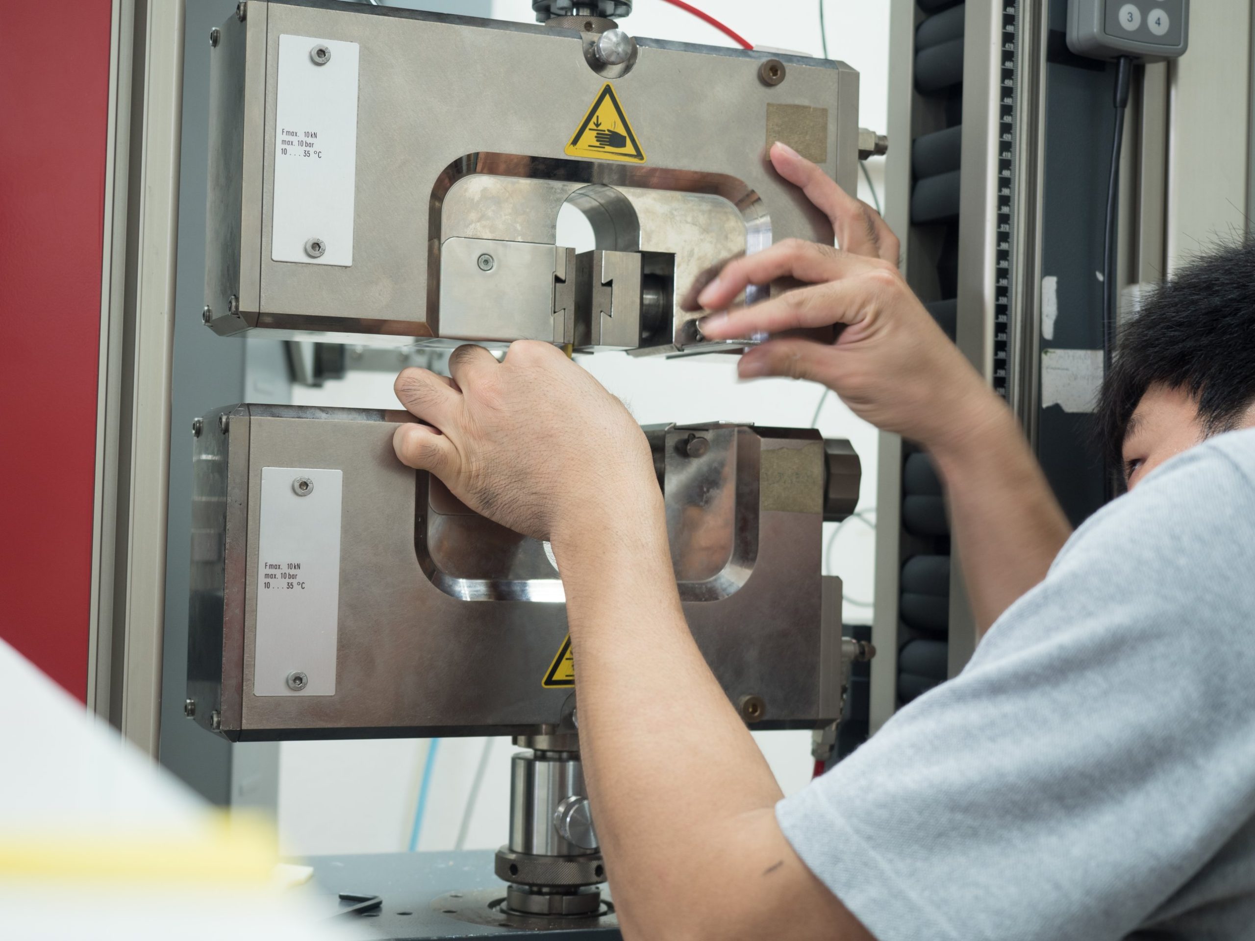 Technician loading a test specimen into the grips of a universal testing machine.