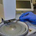 Gloved technician loading a sample pan into a differential scanning calorimeter autosampler.