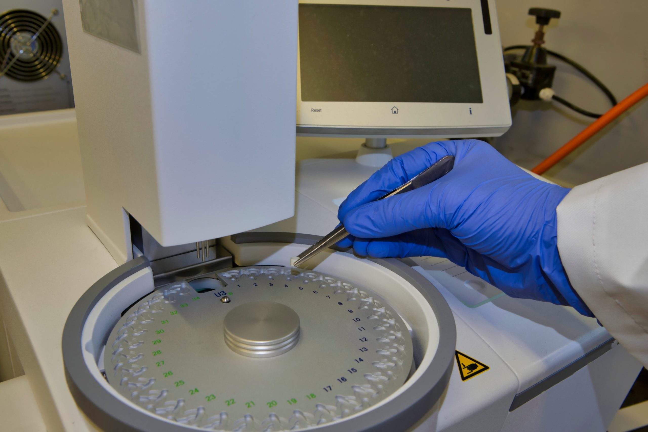 Gloved technician loading a sample pan into a differential scanning calorimeter autosampler.